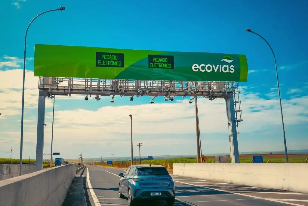 Rodovia com carros passando sob um pórtico de pedágio eletrônico, com placas